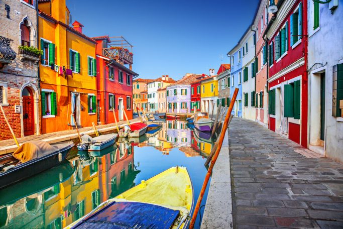 Canal rodeado de casas coloridas en Burano, Venecia, con botes amarrados.