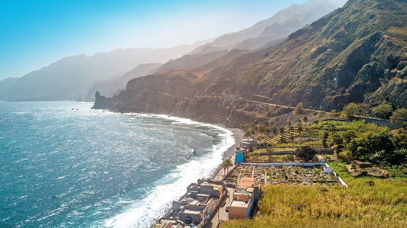Costas rocosas con aguas azules y montañas verdes al fondo.