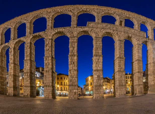Acueducto romano en Segovia, iluminado al atardecer con un cielo azul.