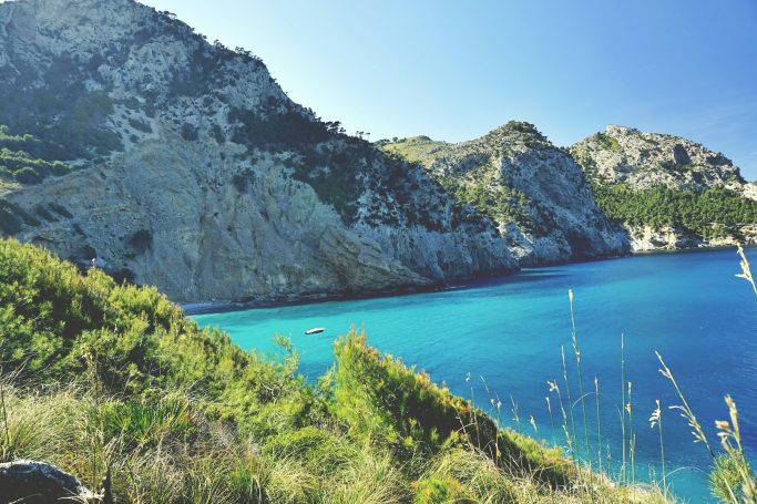 Vista de una playa de aguas turquesas rodeada de montañas y vegetación.